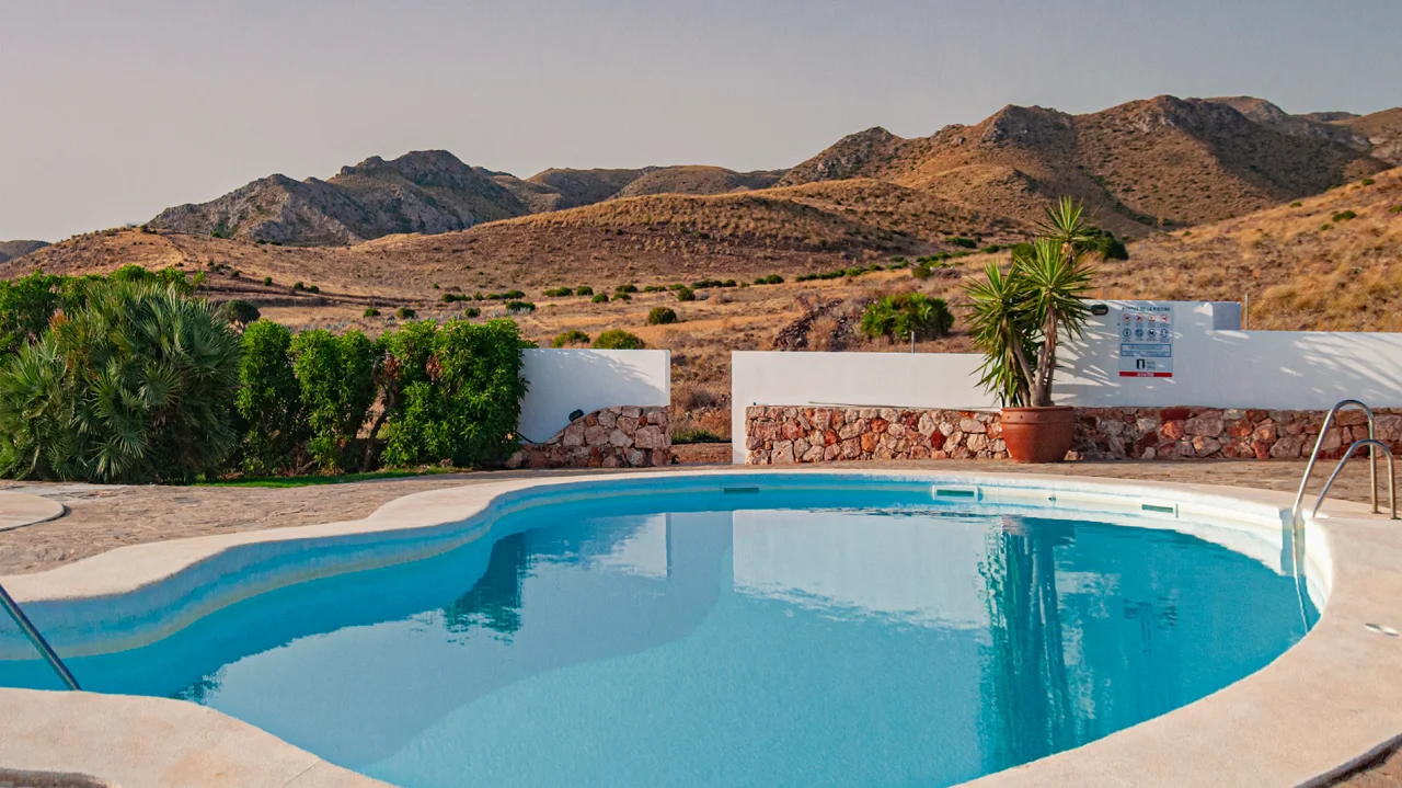 Piscina con paisaje de colinas &aacute;ridas al fondo y plantas tropicales alrededor.