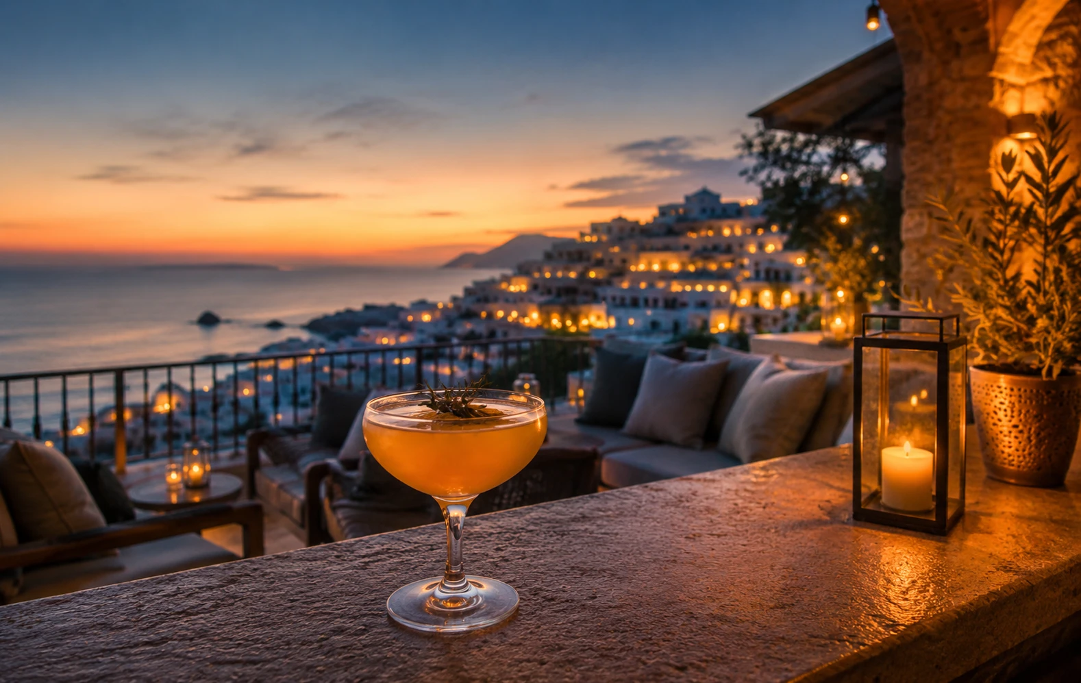 Atardecer en terraza con c&oacute;ctel, velas y vista al mar iluminado.