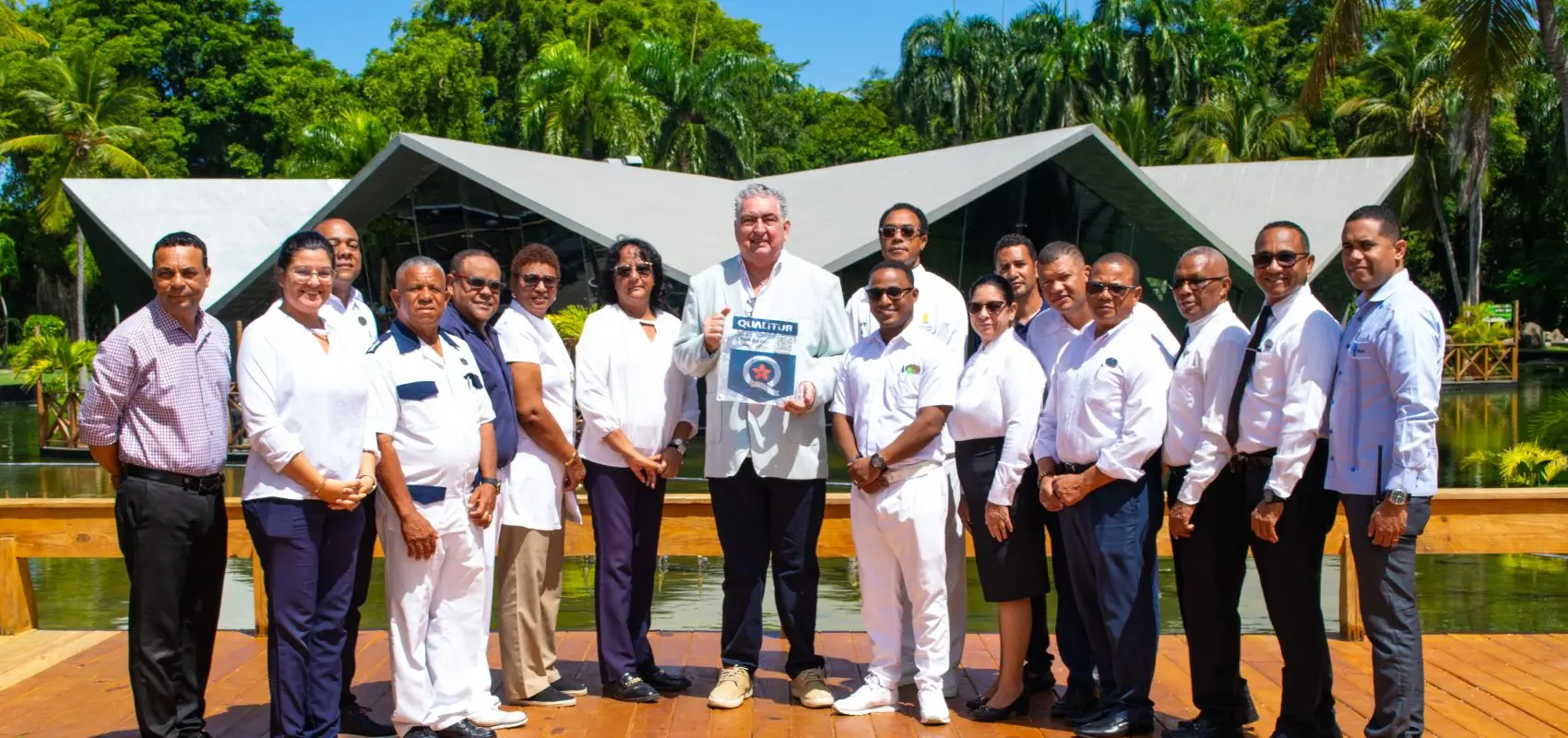 Grupo de personas en uniforme con un premio, frente a edificio con palmeras.
