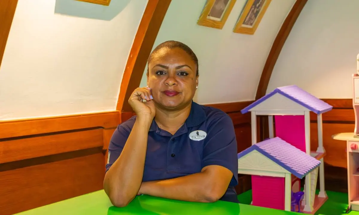 Mujer sonriente posando en interior con casa de juguete de colores.