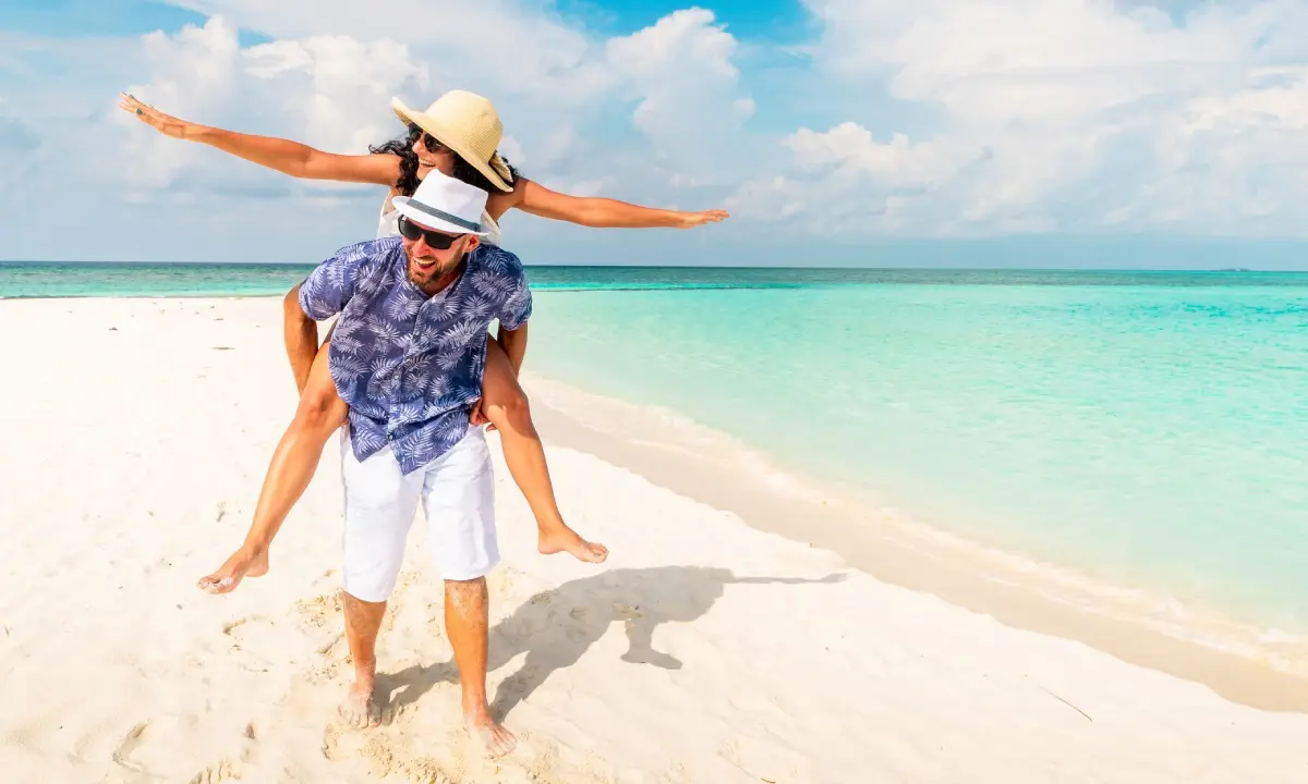 Pareja bailando y sonriendo en la playa, con sombrero y cielo despejado
