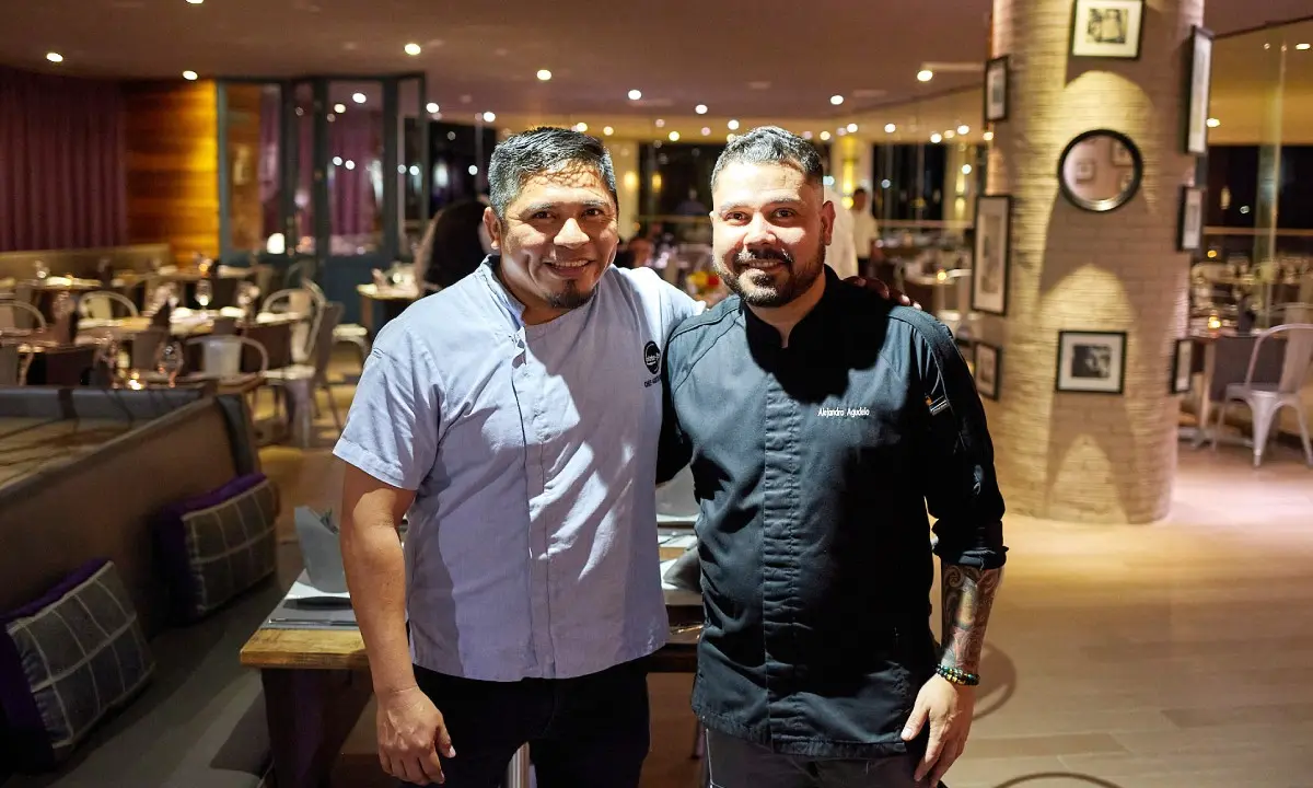 Dos chefs sonrientes en un restaurante, junto a mesas y luces interiores