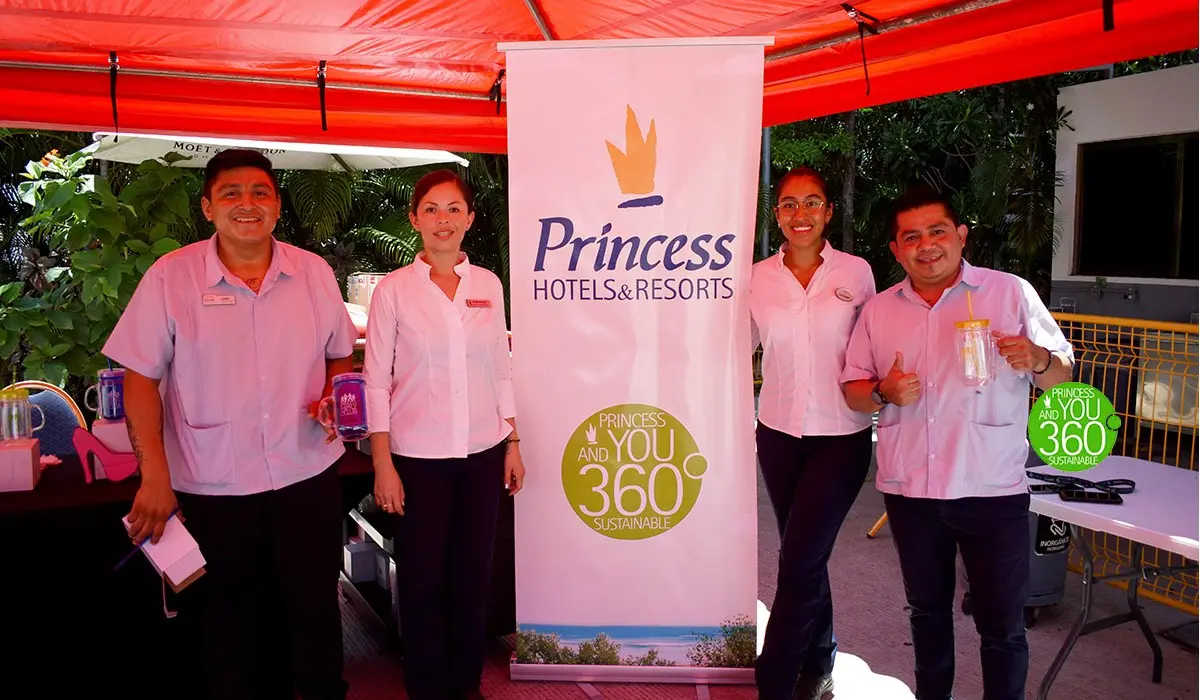 Equipo de hotel Princess Hotels bajo carpa roja, junto a un banner y mesa.