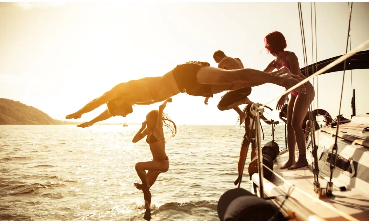 Personas haciendo un salto en el mar desde un velero al atardecer