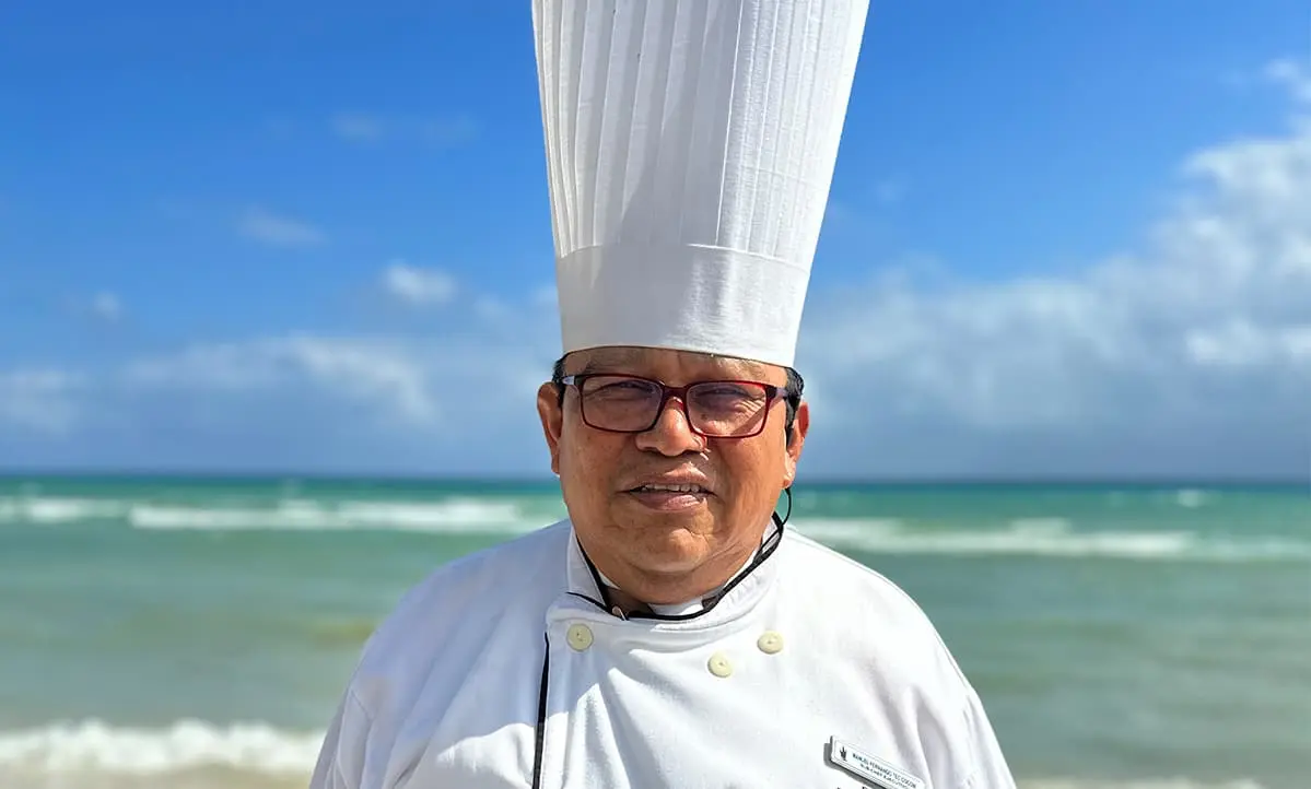 Chef con gorro blanco y lentes, frente al mar azul y cielo nublado