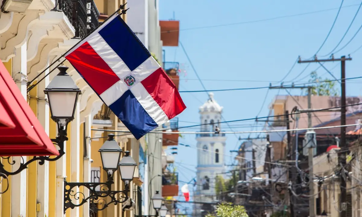 Bandera de Rep&uacute;blica Dominicana ondeando en una calle con edificios y cables el&eacute;ctricos