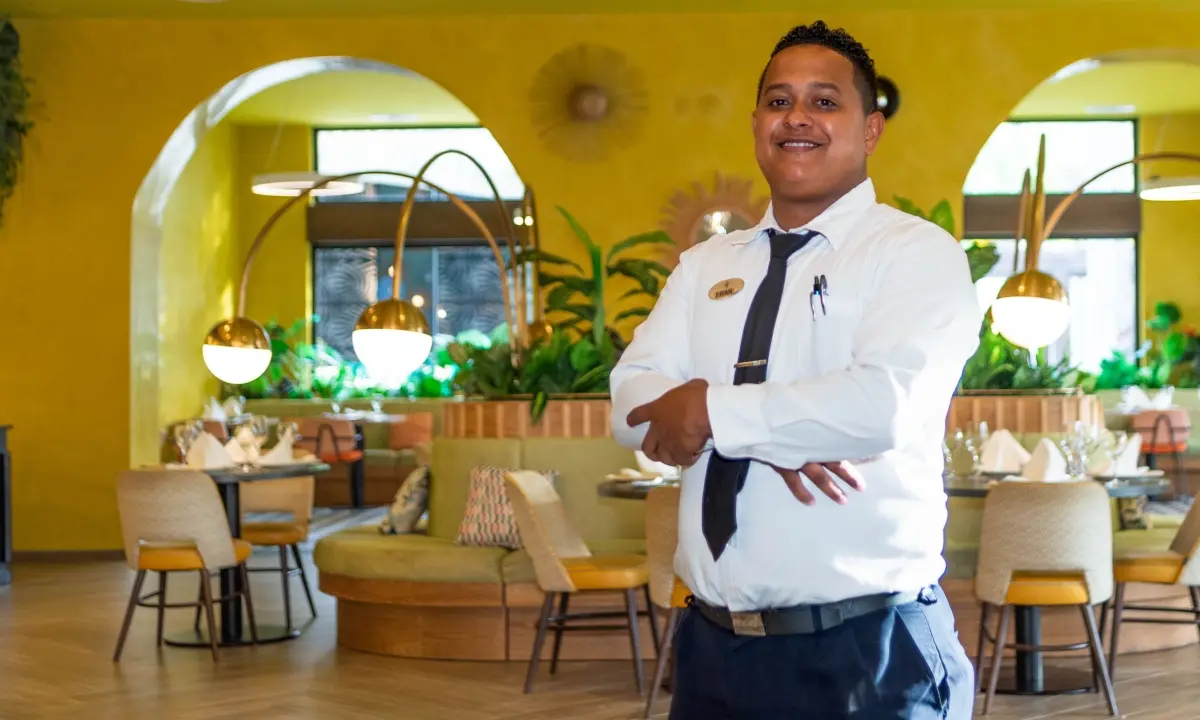 Camarero con camisa blanca y corbata en un restaurante amarillo