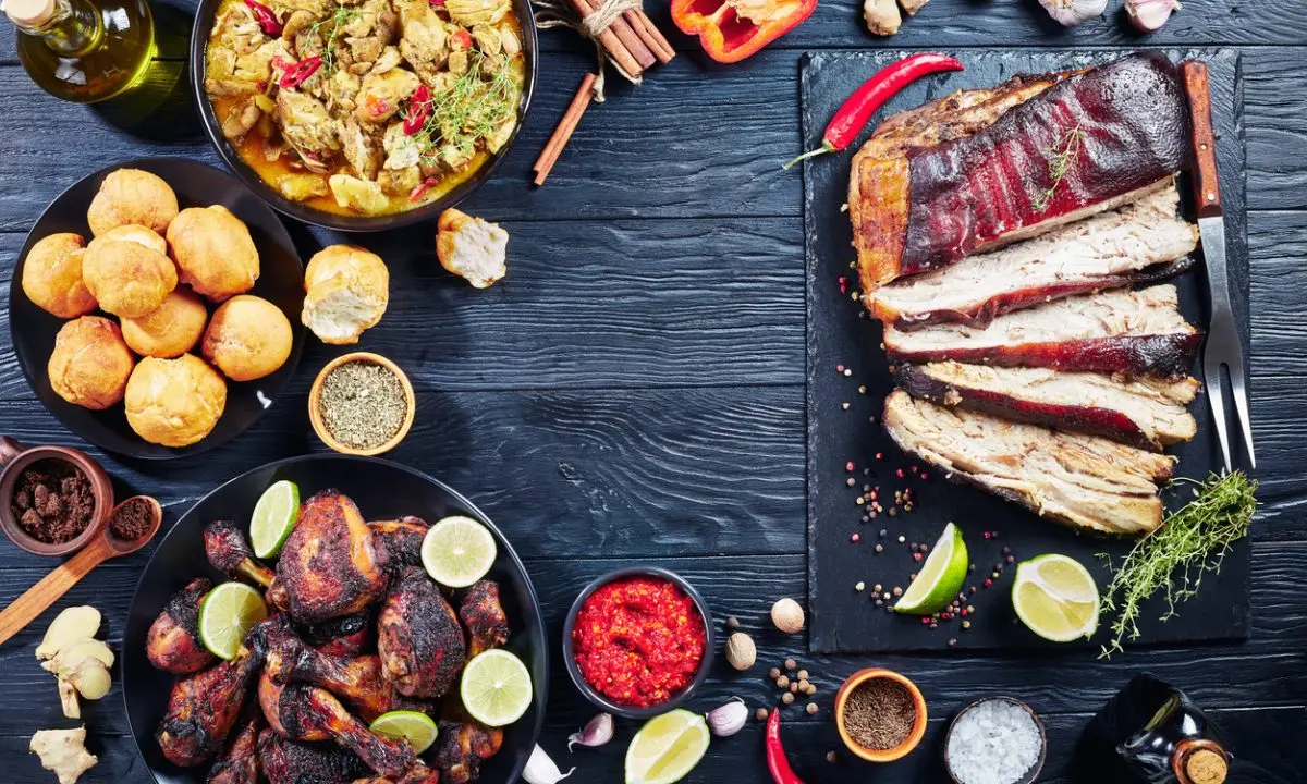 Mesa con costillas asadas, plato con salsa y papas sobre fondo oscuro