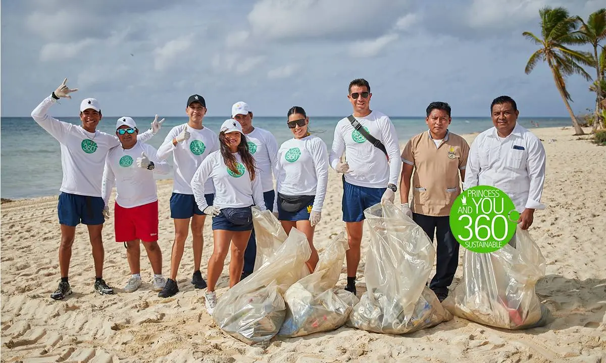 Grupo de voluntarios con playeras &ldquo;360&rdquo; recogiendo basura en la playa.