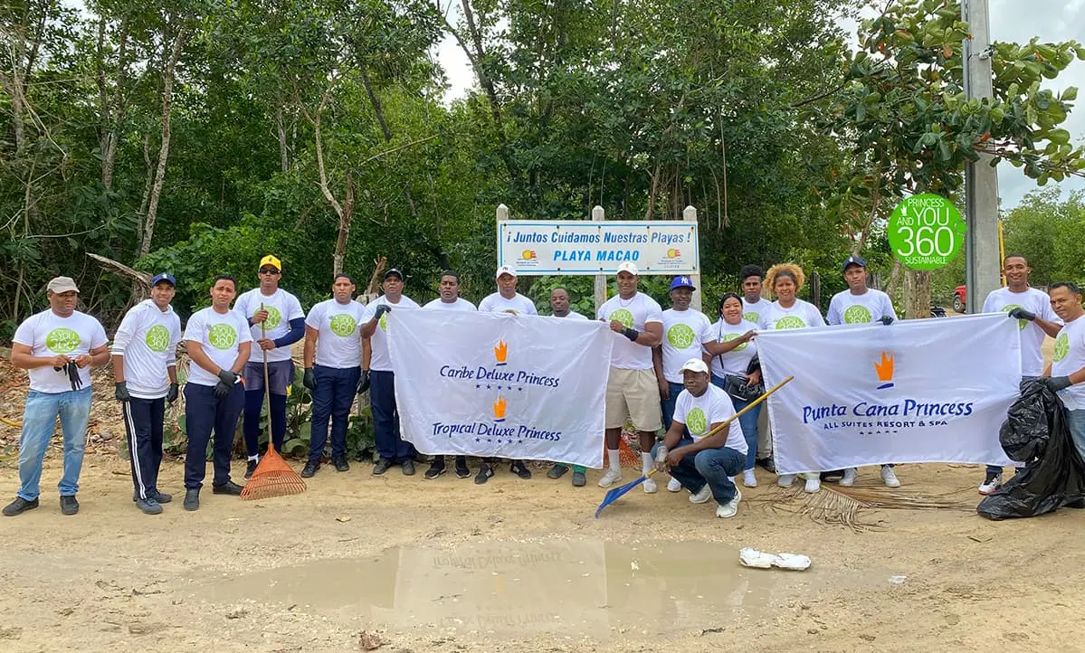 Grupo de voluntarios con pancartas y banderines, limpiando la playa al aire libre.