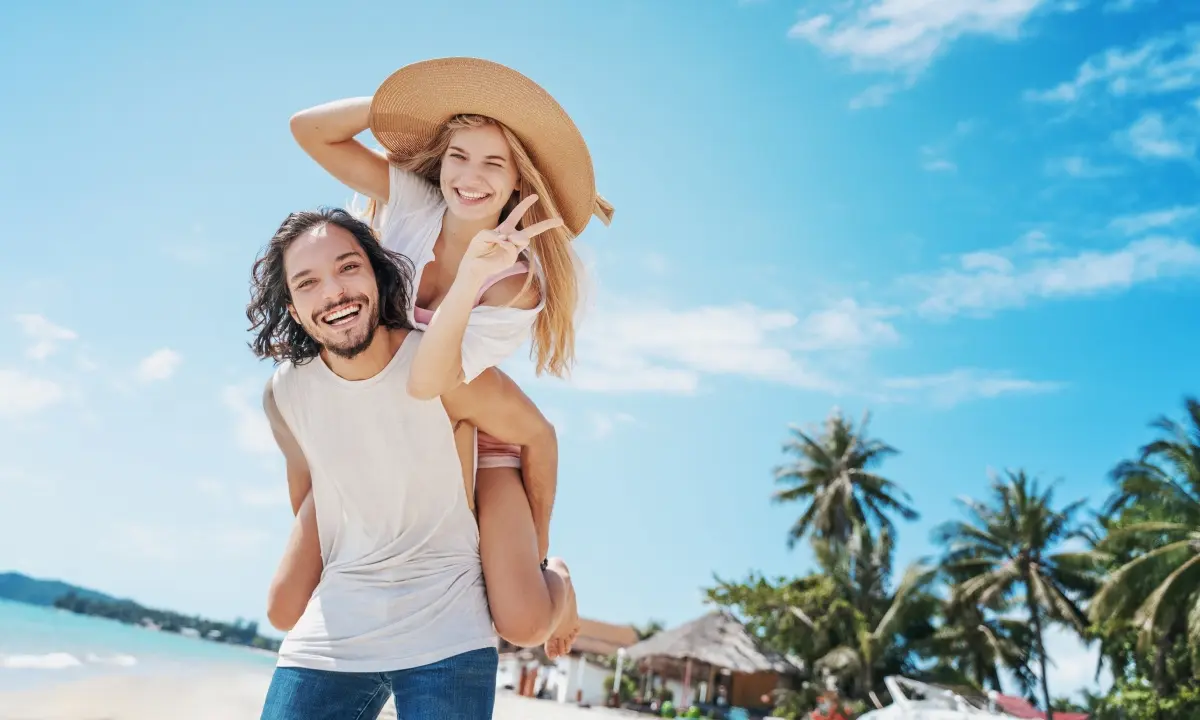 Pareja sonriente bailando en la playa con palmeras y cielo azul