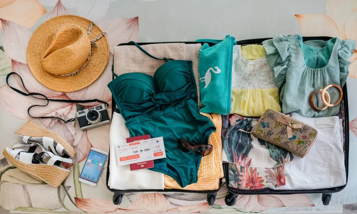 Maleta abierta con ropa y accesorios de viaje: ba&ntilde;ador, prendas y sombrero.