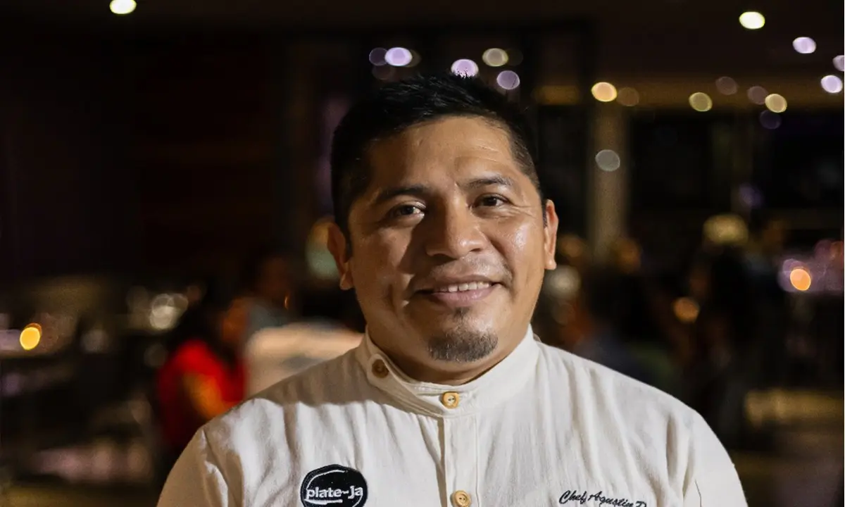 Retrato de hombre sonriendo con camisa blanca en un ambiente nocturno con luces.