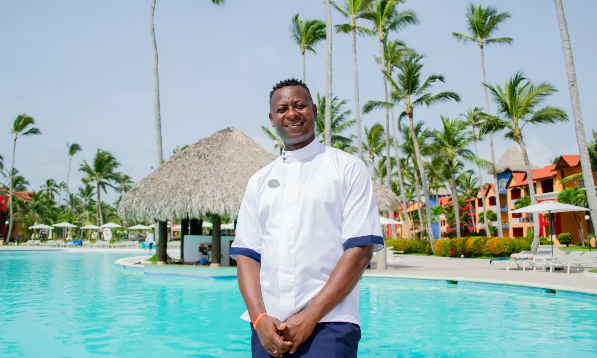 Chef sonriente frente a piscina con palmeras y caba&ntilde;as en resort tropical