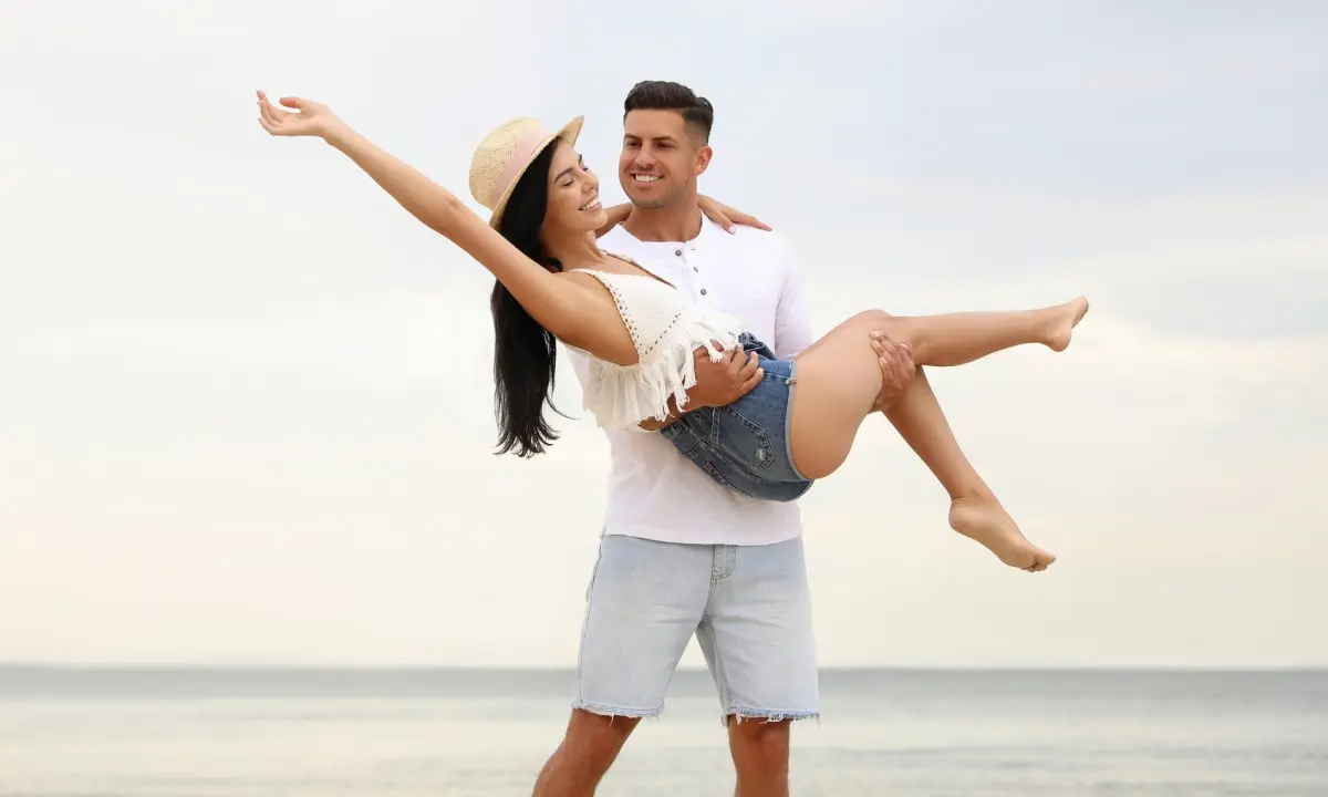 Pareja bailando en la playa al atardecer, el hombre levanta a la mujer