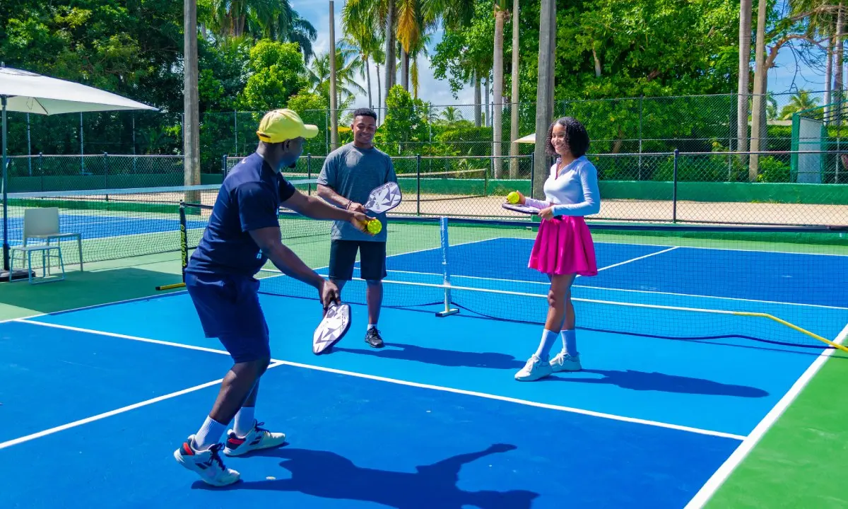 Personas jugando p&aacute;del en una cancha al aire libre, con palas y pelota.