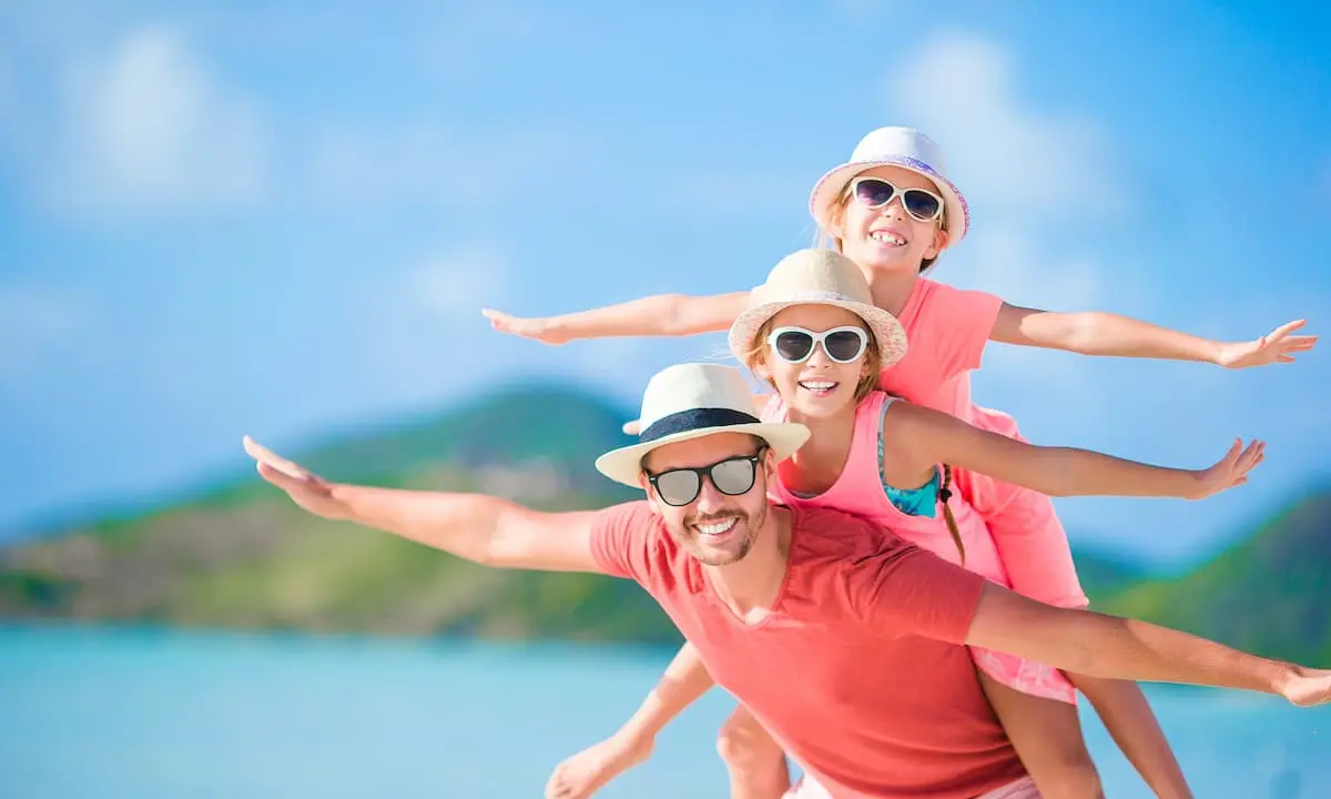 Familia sonriendo y con sombreros en playa, brazos abiertos contra el mar