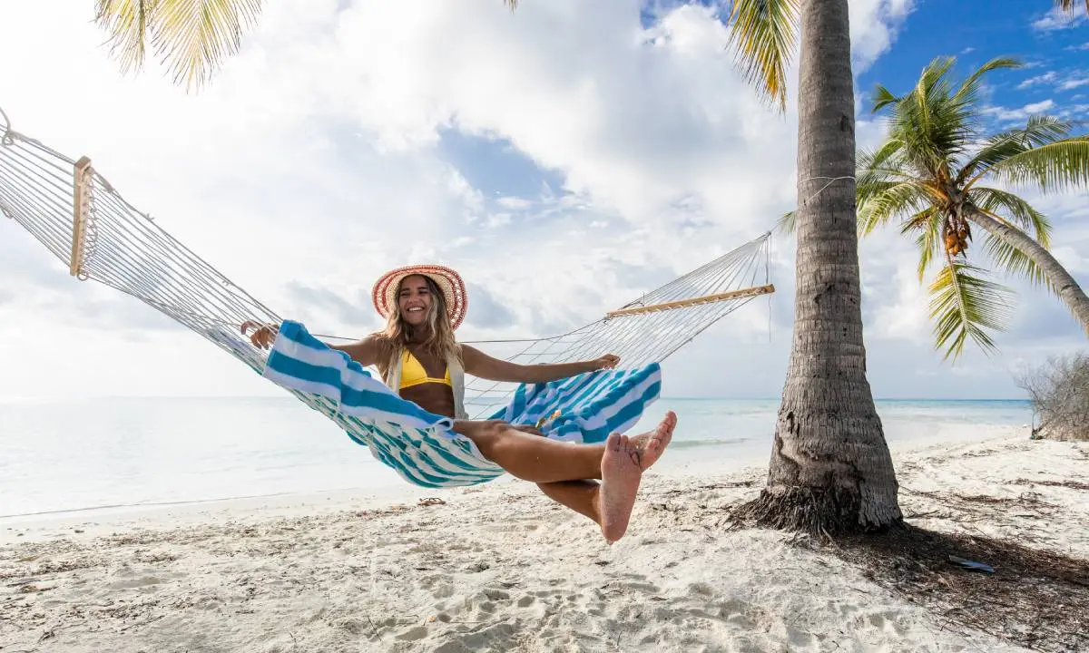 Mujer sonriente en hamaca colgante en playa tropical con palmeras