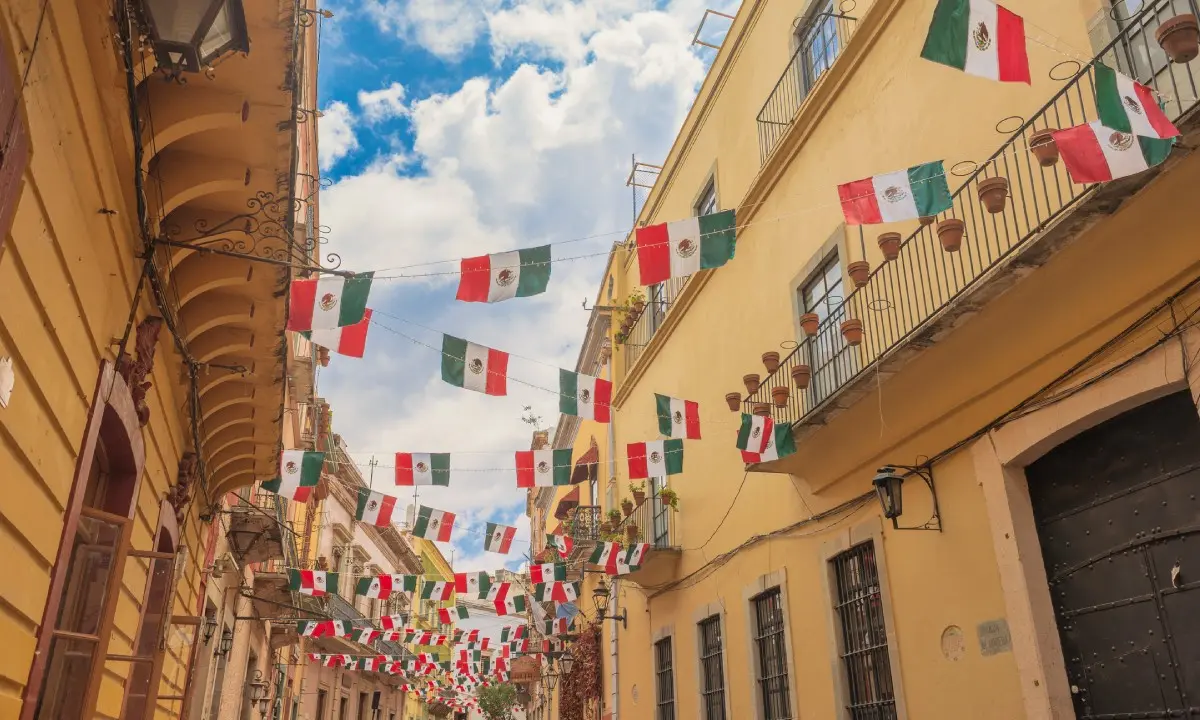 Banderas de M&eacute;xico ondeando entre edificios coloniales y cielo nublado