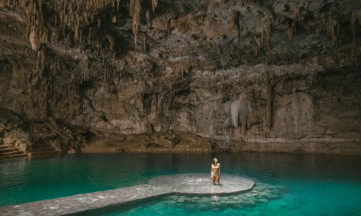 Mujer de pie en un jacuzzi natural de agua turquesa bajo una cueva con estalactitas