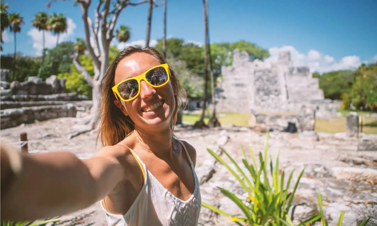 Mujer sonriente con gafas amarillas en ruinas antiguas bajo el sol