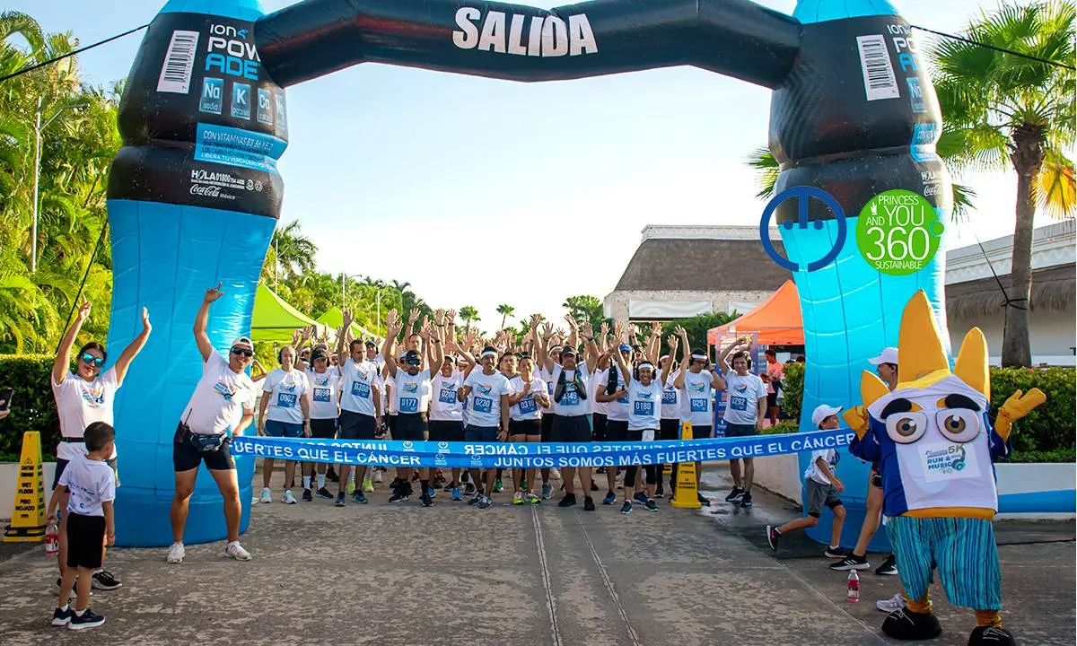 Participantes en carrera solidaria bajo un arco inflable &ldquo;Salida&rdquo; con palmeras y p&uacute;blico