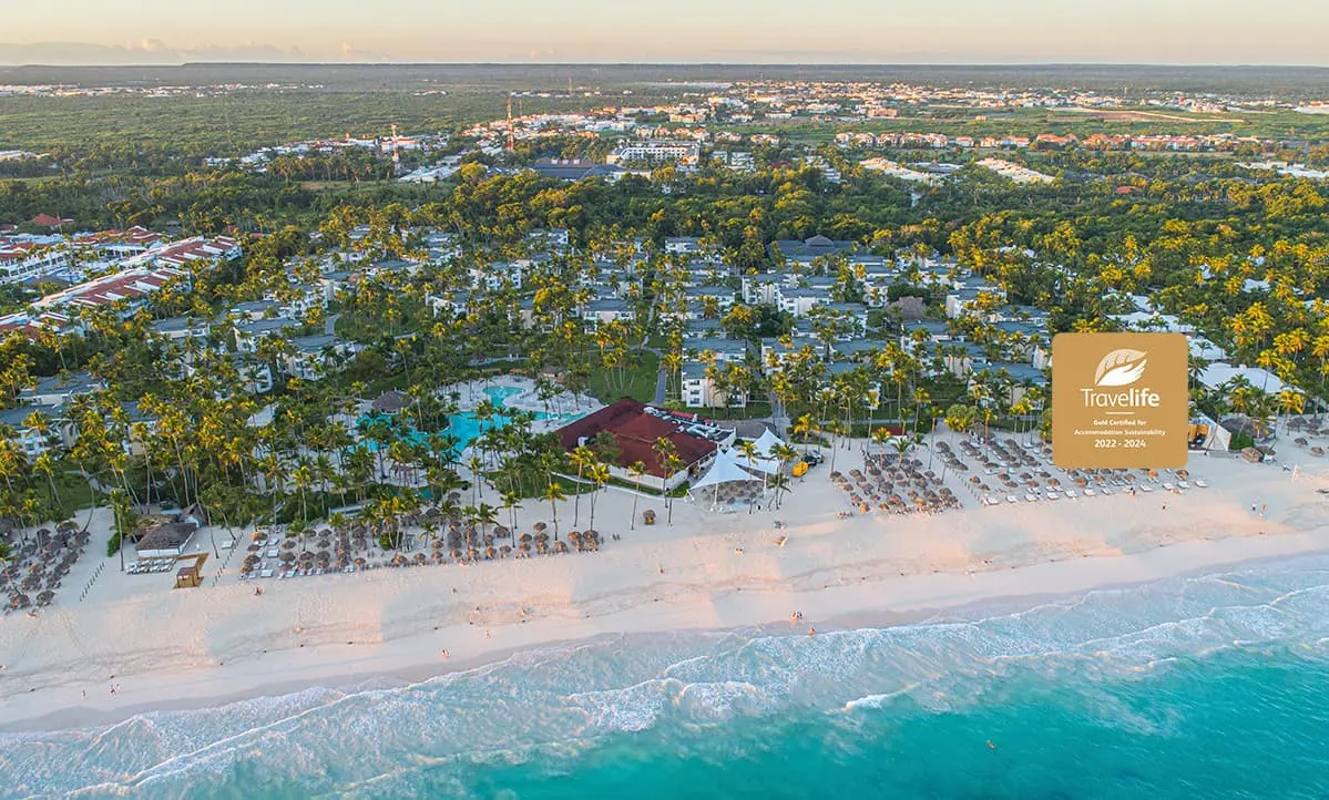 Vista a&eacute;rea de un hotel junto a la playa, con palmeras y logo Travelife.