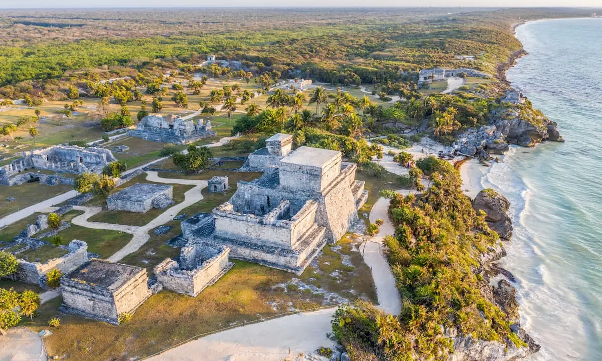 Vista a&eacute;rea de ruinas mayas junto al mar, con vegetaci&oacute;n y senderos entre ellas