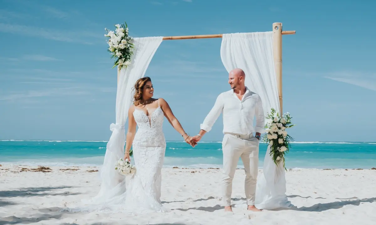 Boda en la playa: pareja de novios con arco y flores, junto al mar