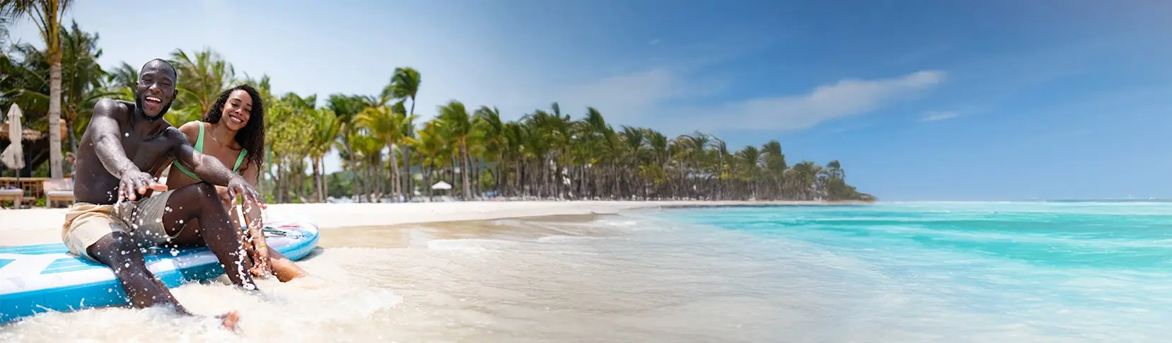 Pareja en la playa tropical con palmeras y mar turquesa, jugando en el agua