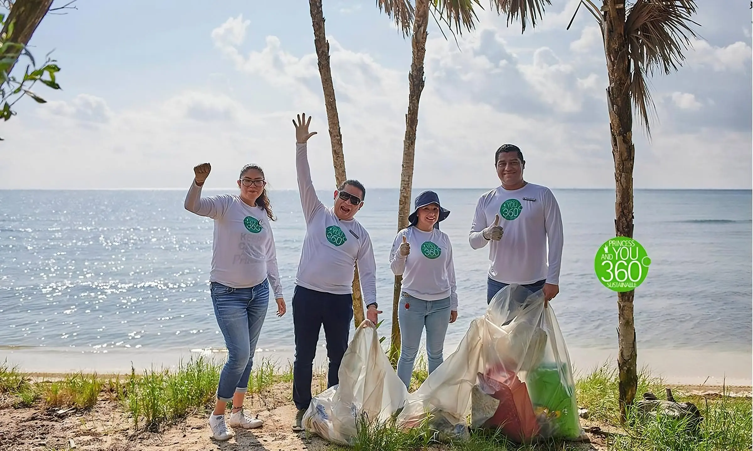 Cuatro personas con playeras &ldquo;360&rdquo; limpian la playa; alzan la mano junto al mar