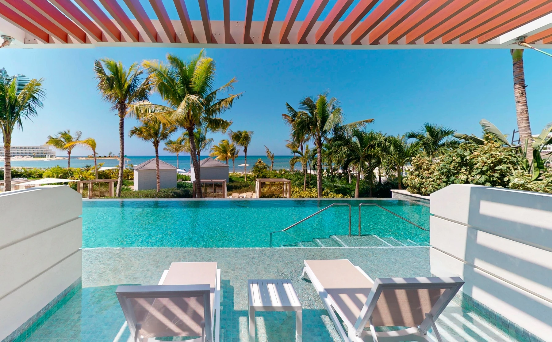 Piscina frente al mar con palmeras y tumbonas, cielo despejado