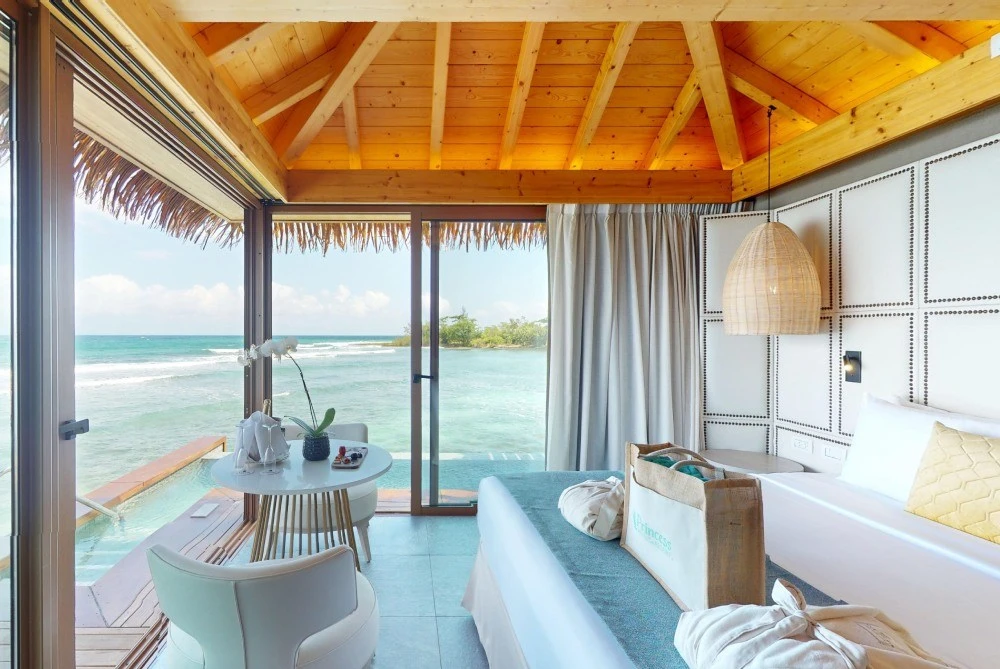 Interior de caba&ntilde;a frente al mar, con cama, cortinas y terraza acristalada