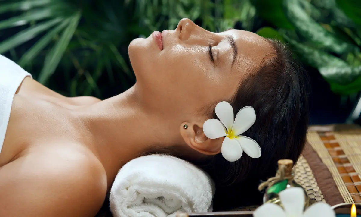 Mujer relajada en spa con flor blanca y fondo verde, recostada sobre toalla