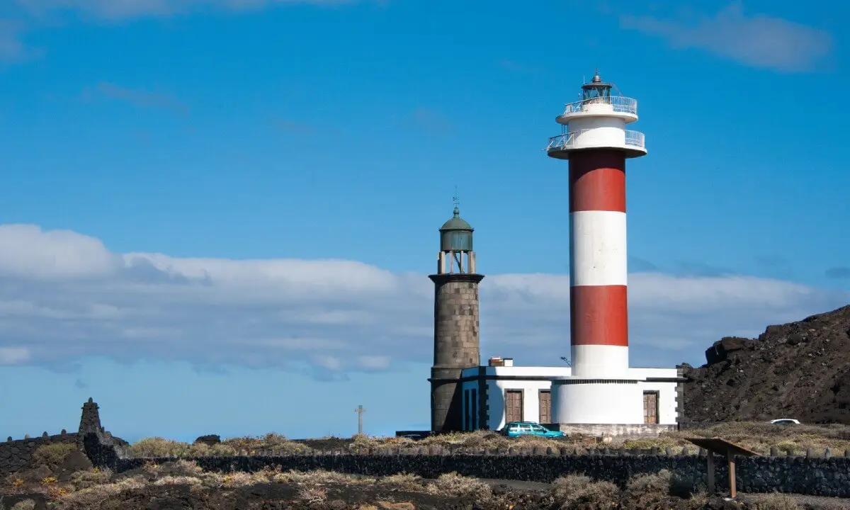 Faro rojo y blanco con edificios junto al mar, cielo nublado