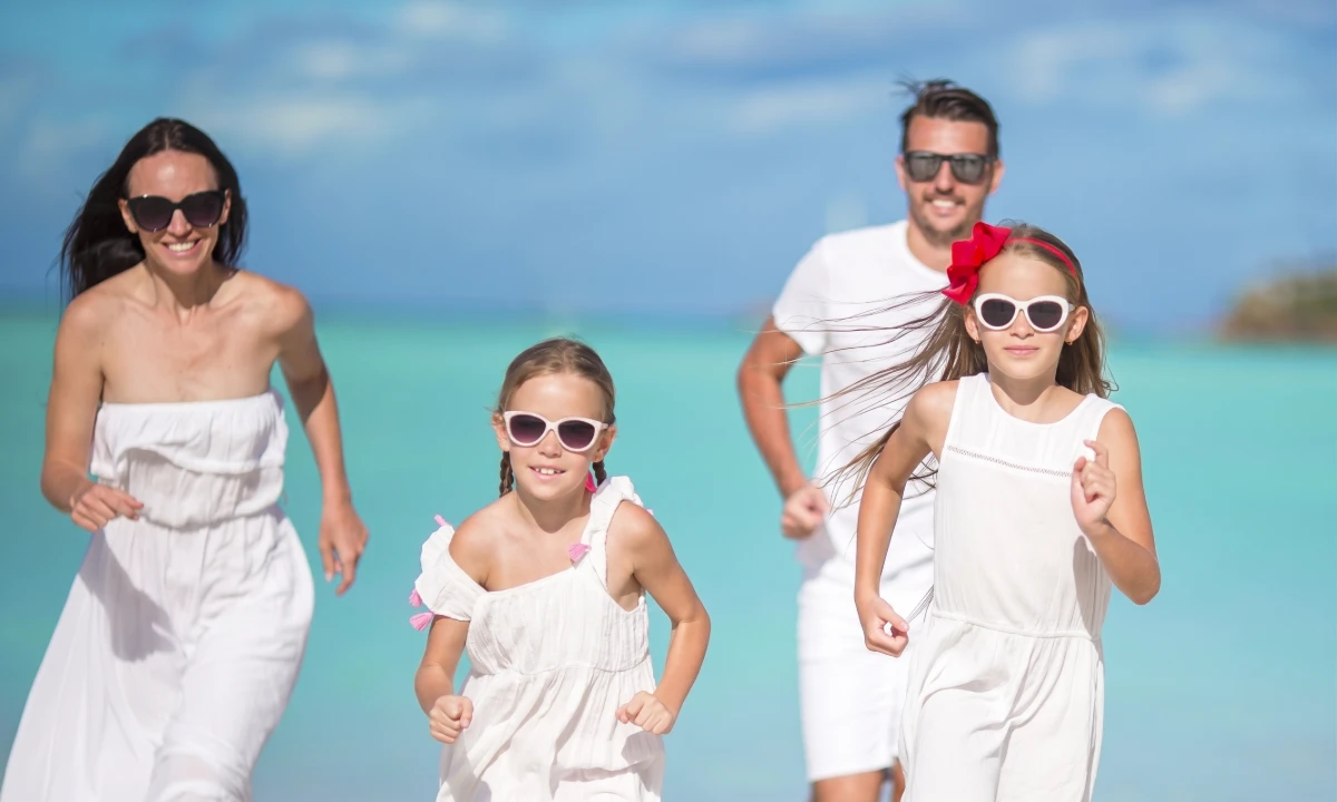 Familia en la playa corriendo, todos con gafas de sol y ropa blanca