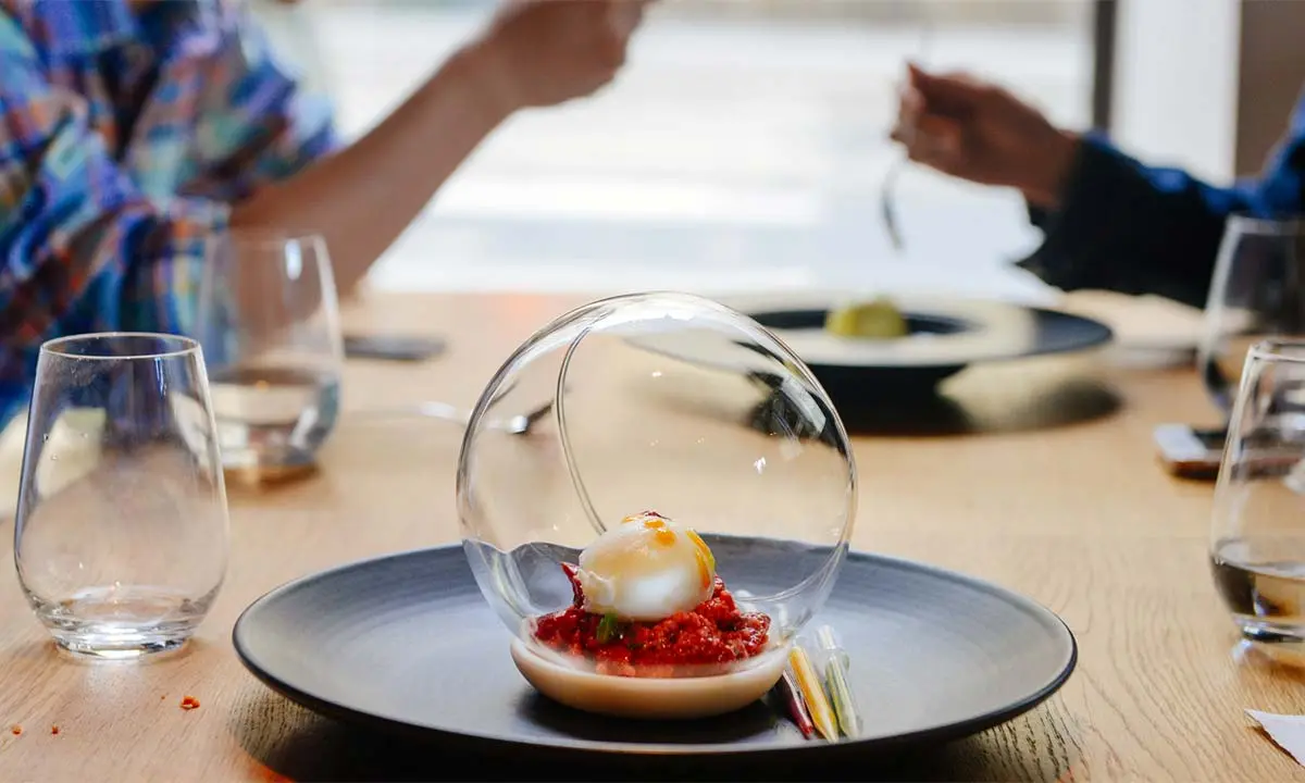 Plato con huevo y esfera de cristal en mesa, manos al fondo.