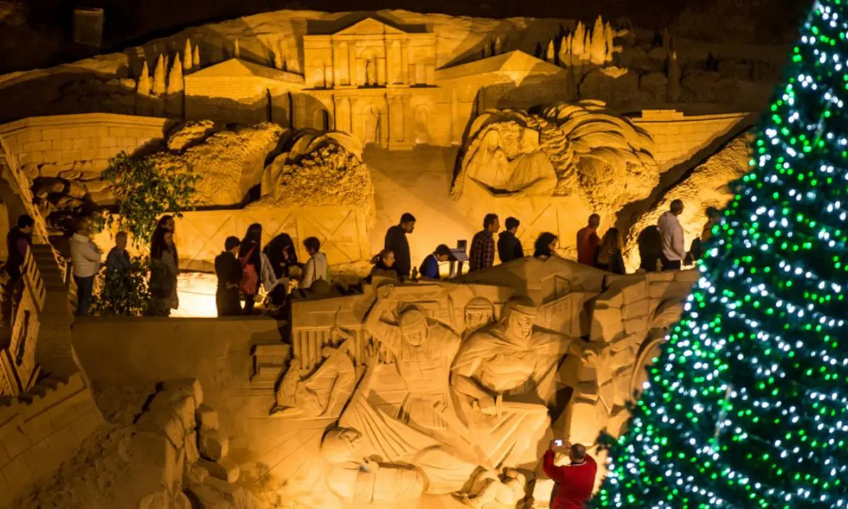 Personas visitan un bel&eacute;n iluminado con un &aacute;rbol de Navidad al atardecer