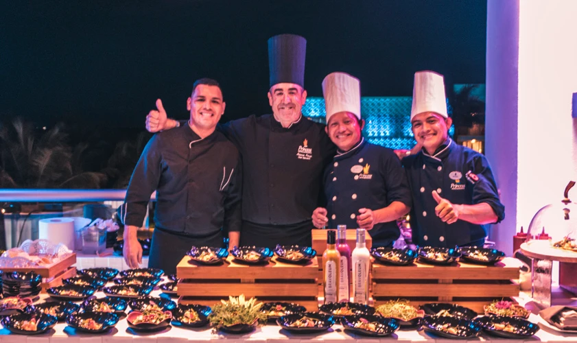 Cocineros con uniformes posan junto a parrillas y platos en un evento.