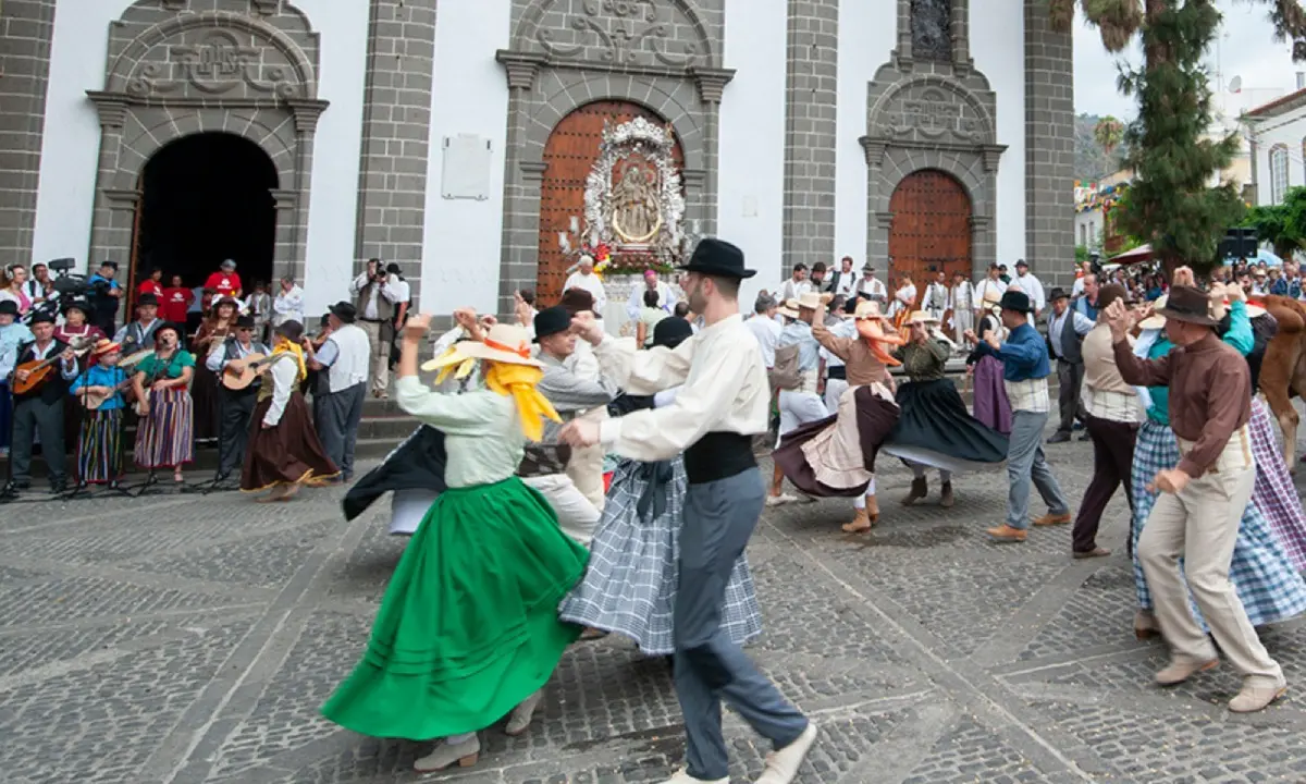 Baile folcl&oacute;rico con parejas y m&uacute;sica frente a una iglesia de piedra.
