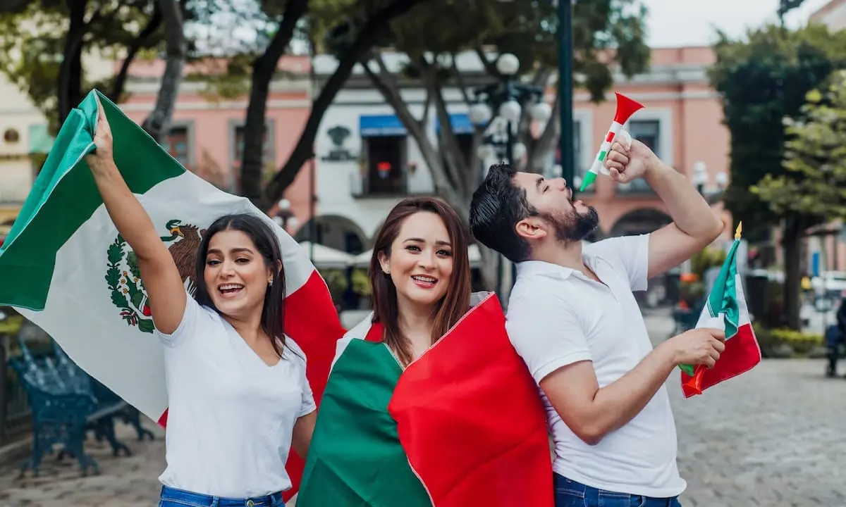 Tres j&oacute;venes con banderas mexicana y tricolor, celebran en la calle.