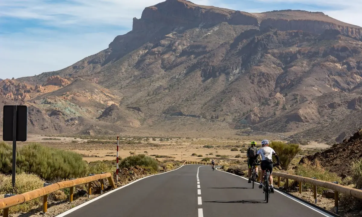 Ciclistas pedaleando por carretera entre monta&ntilde;as y valle des&eacute;rtico