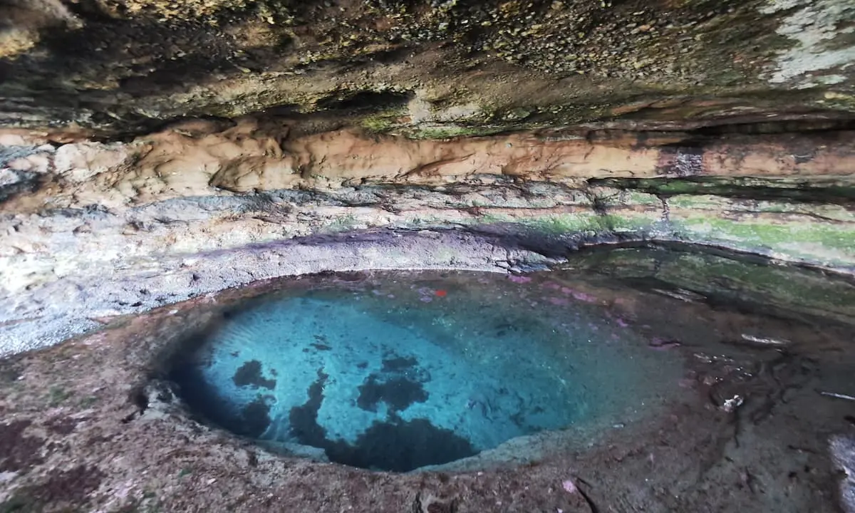 Pozo de agua azul en una cantera con paredes de roca y musgo.