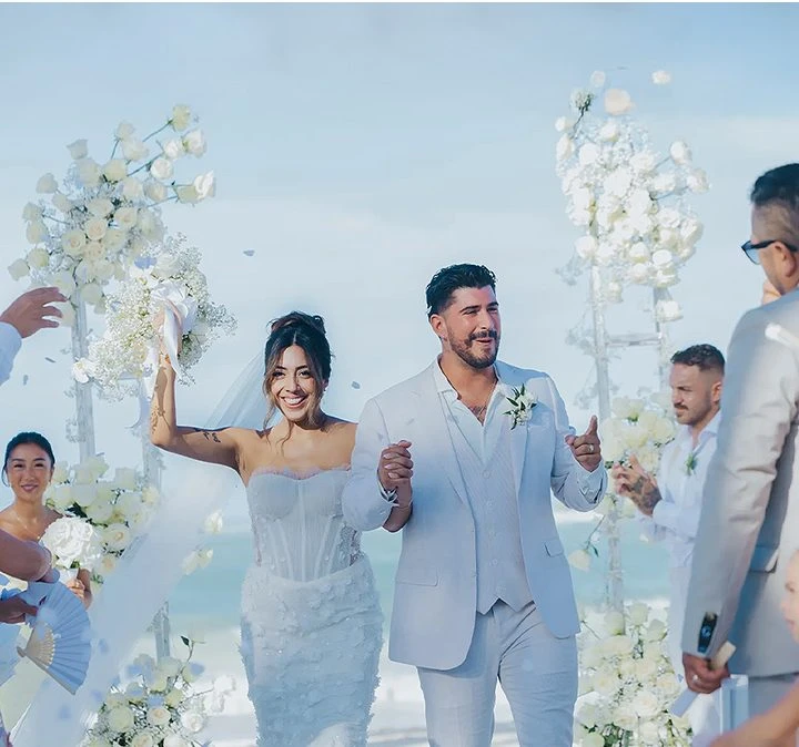 Pareja de novios en ceremonia, con flores blancas y amigos al lado