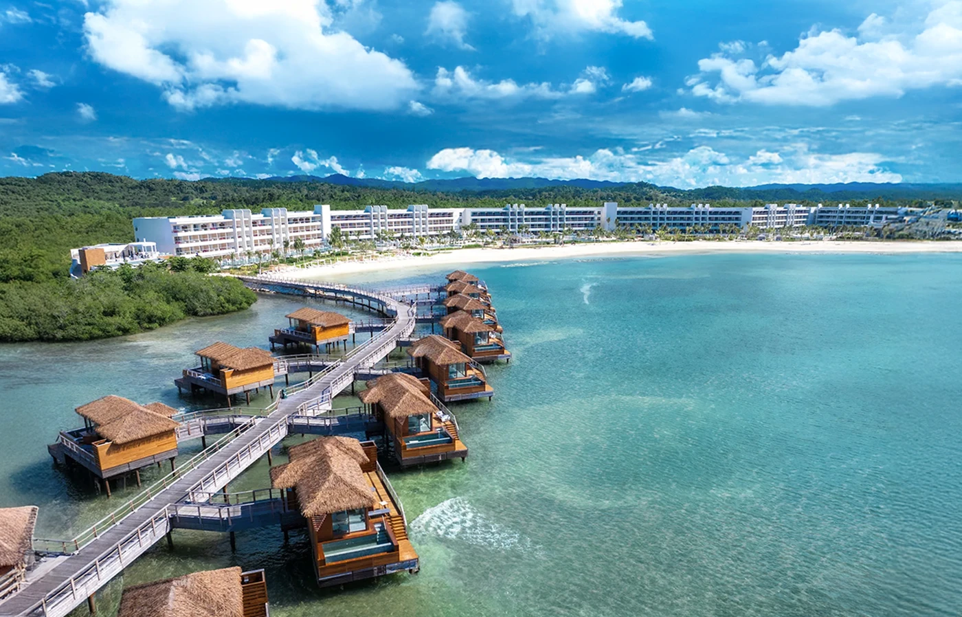 Hotel junto a playa tropical, muelle y caba&ntilde;as sobre el agua, cielo azul