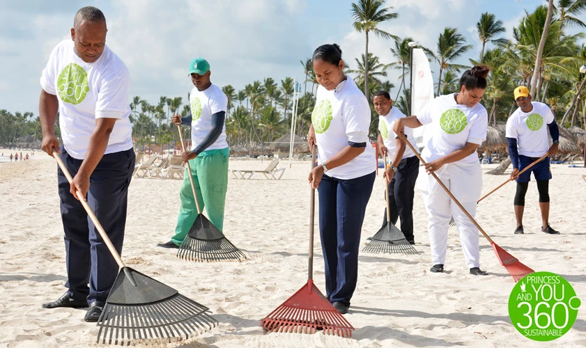 Personas voluntarias en la playa barren arena con escobas y palas.