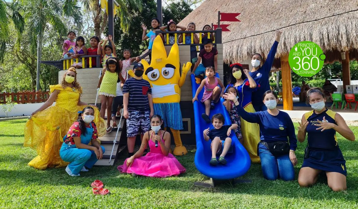 Grupo de ni&ntilde;os y adultos con mascarillas en un evento con personajes inflables.