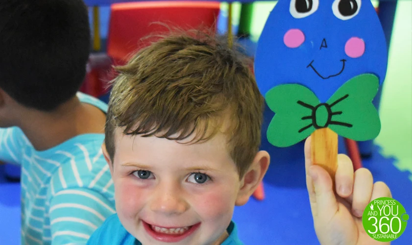 Ni&ntilde;o sonriente con peluche azul de conejo, en aula infantil.