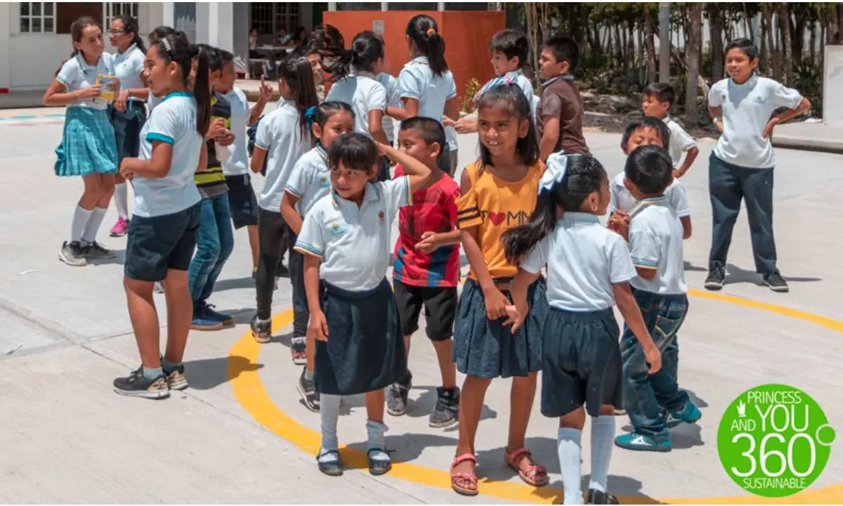 Grupo de ni&ntilde;os en uniforme caminando y jugando en patio escolar al sol.