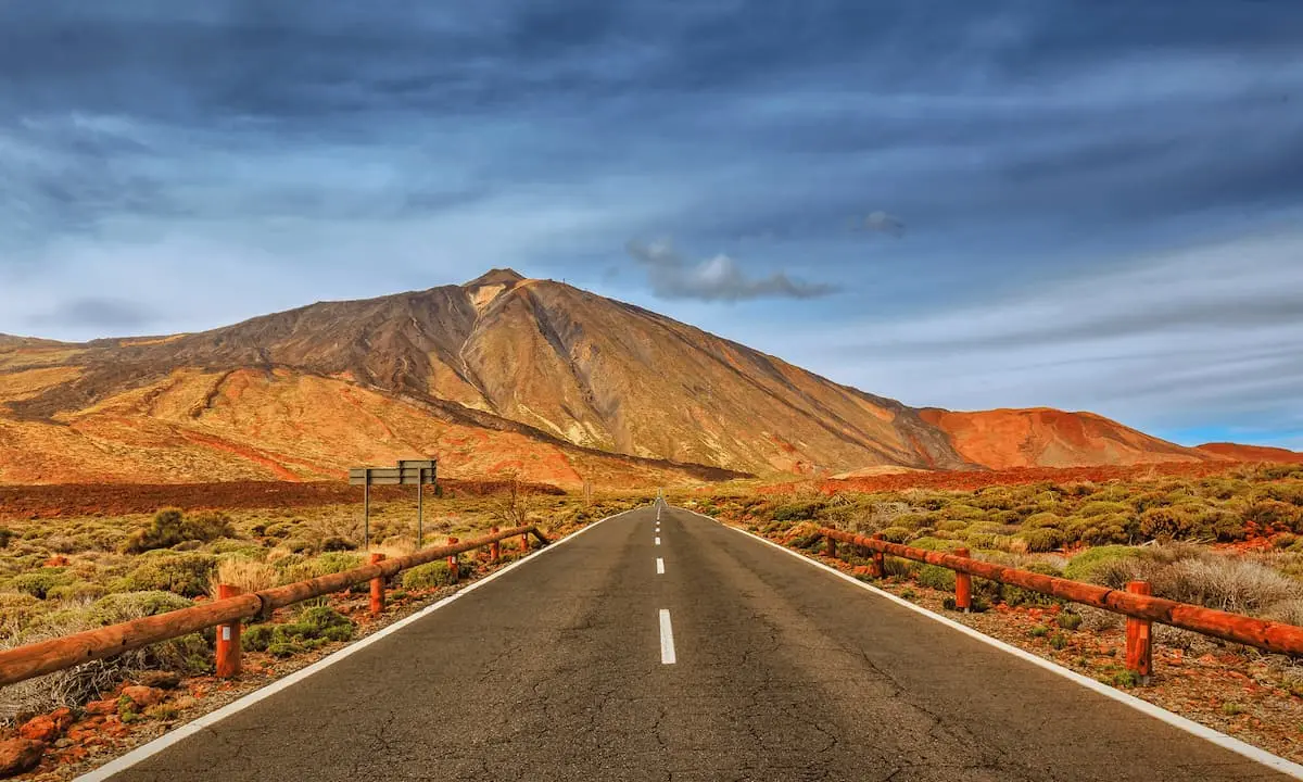 Camino asfaltado hacia monta&ntilde;as coloridas bajo cielo nublado